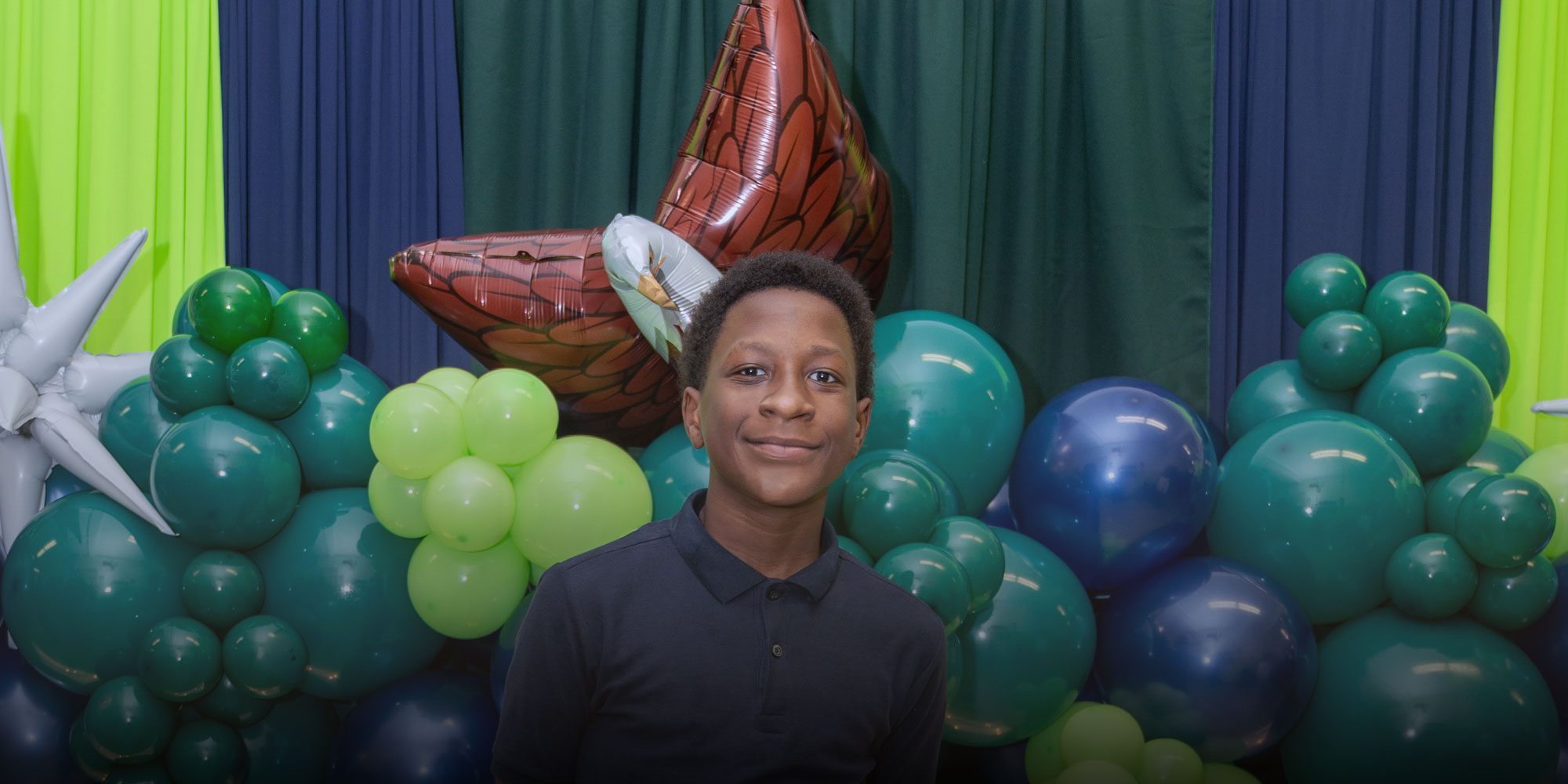 Smiling student in front of green and blue balloons.