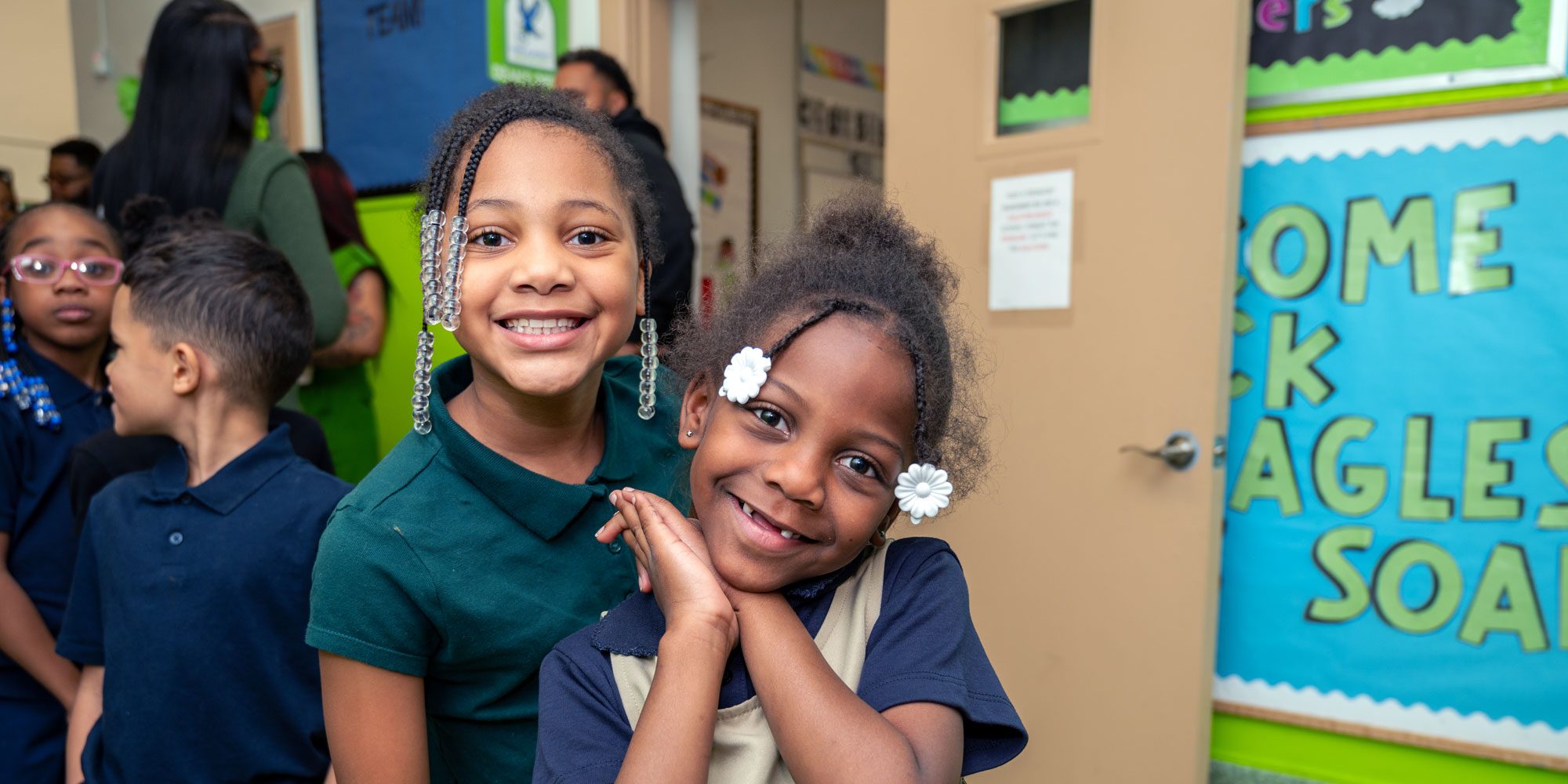 Two smiling students in a school hallway.